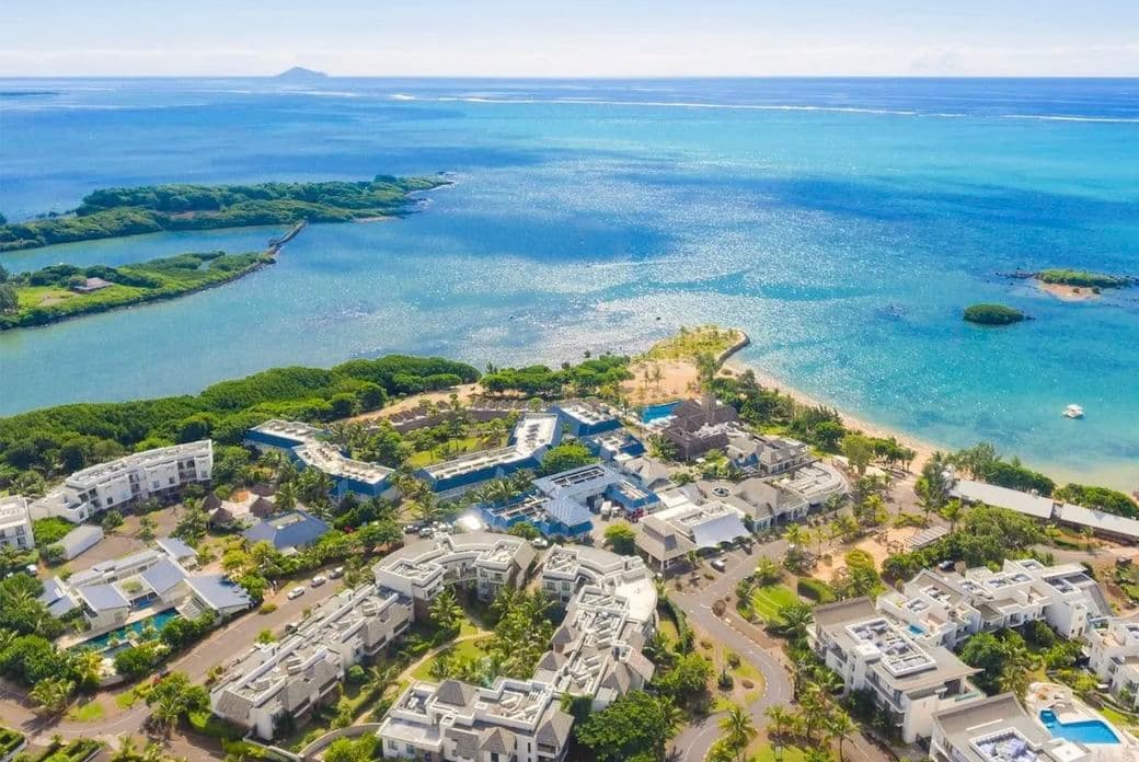 Luftaufnahme des Küstenresorts Haute Rive mit weißen Gebäuden, üppigem Grün und türkisfarbenem Meerwasser unter einem klaren blauen Himmel.
